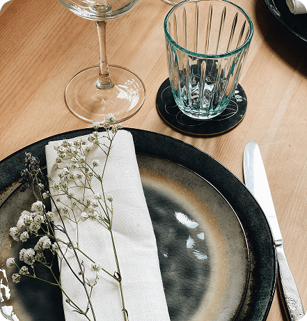 Couvert de table élégant composé d'une assiette en céramique, d'une serviette blanche ornée de brin de gypsophile et de verres à eau et à vin.