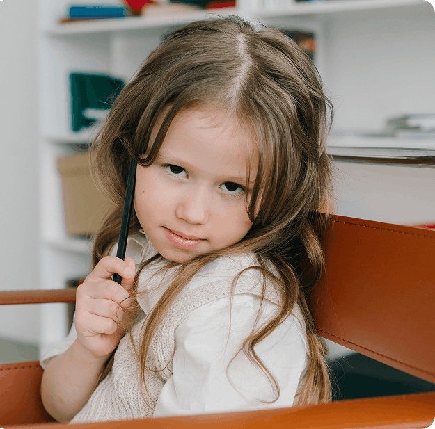 Portrait d'une jeune fille pensive tenant un crayon près de sa joue, assise à un bureau.