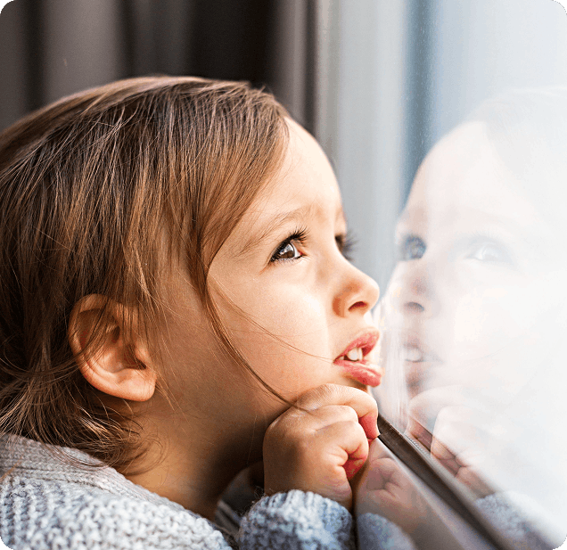Petite fille appuyée contre une vitre, regardant attentivement vers l'extérieur.