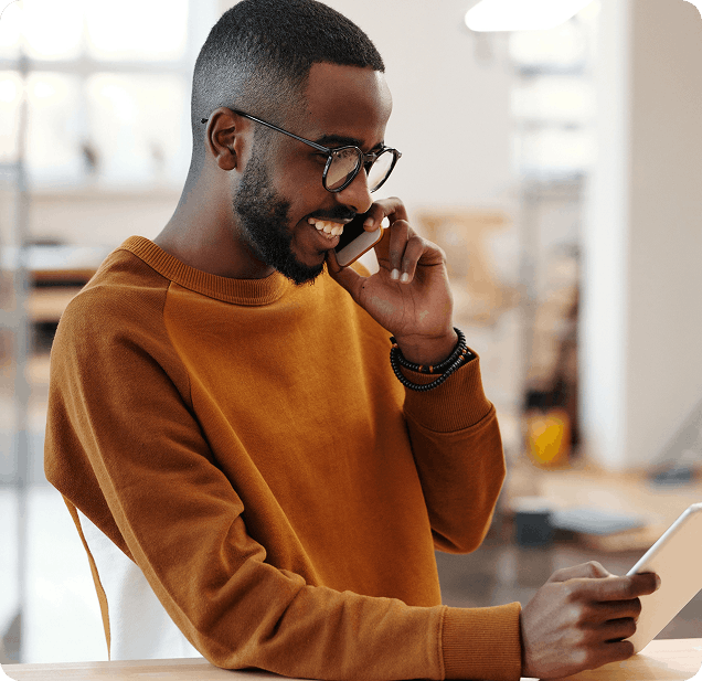 Homme souriant avec des lunettes passant un appel téléphonique tout en consultant une tablette.
