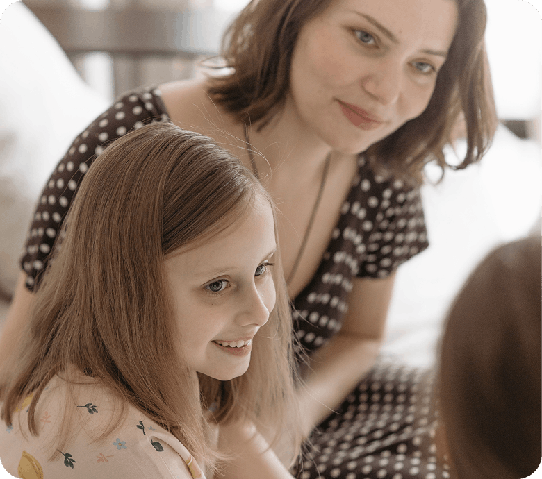 Une mère et sa fille souriantes partageant un moment complice à la maison.